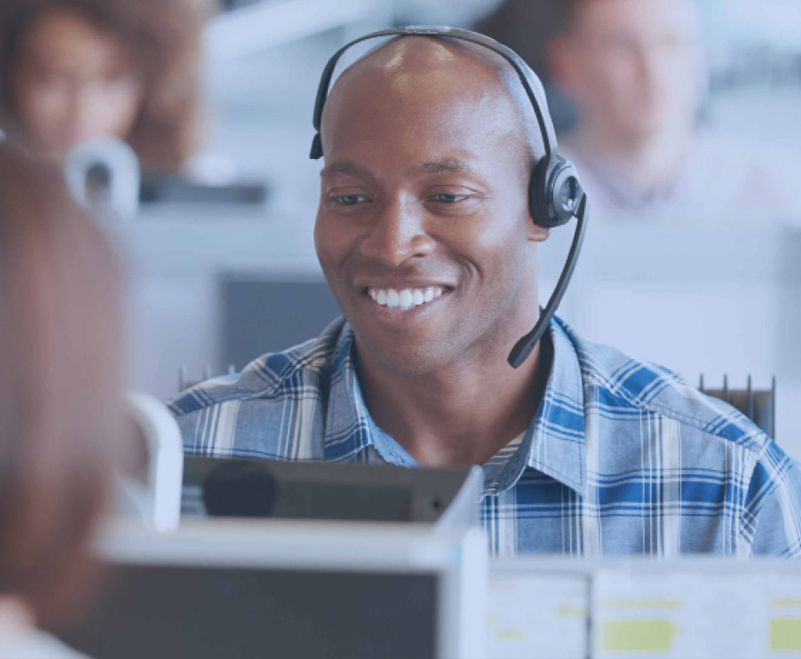 A man in an office wearing a headset, focused on his work, surrounded by a modern workspace and technology.